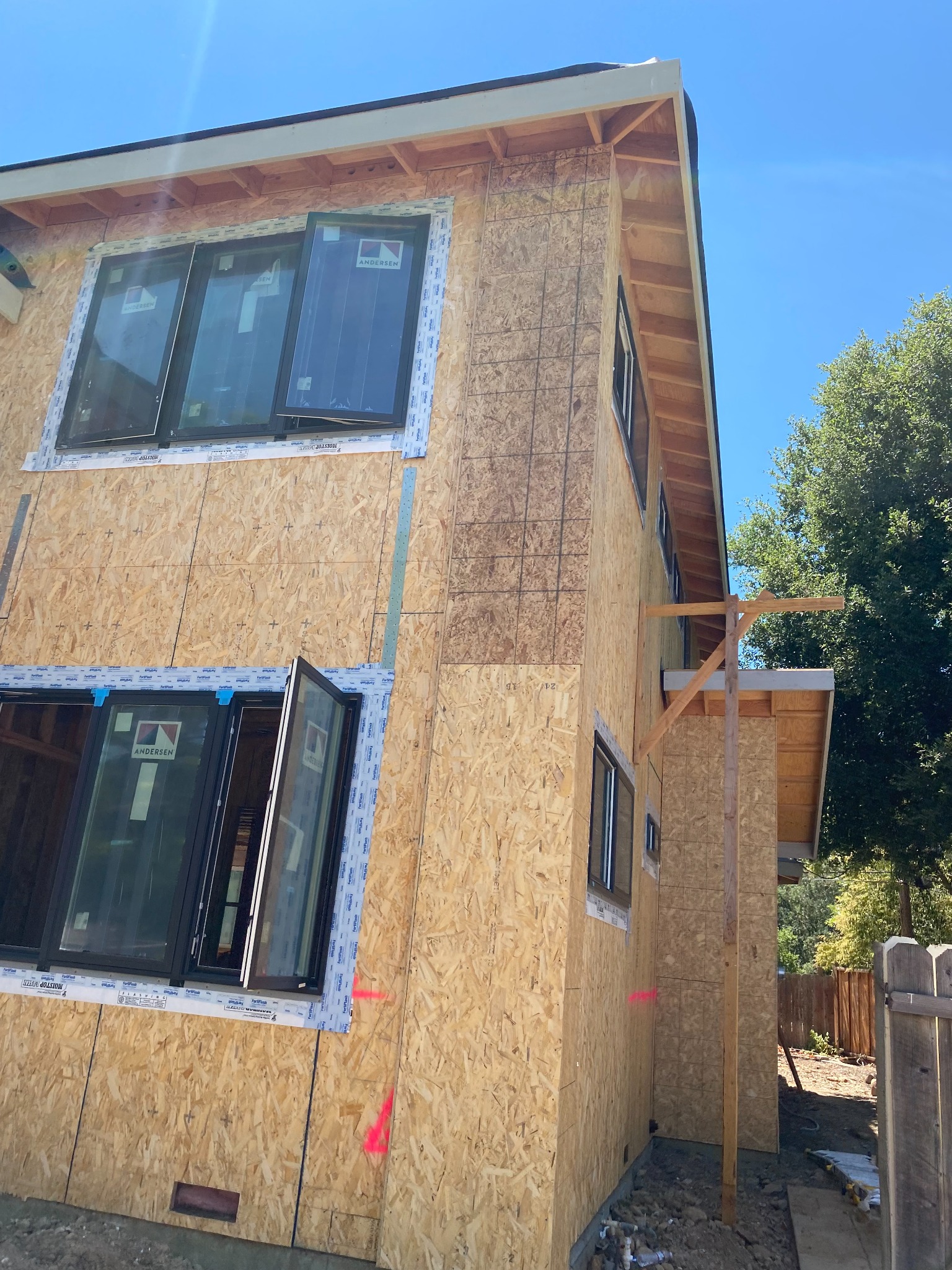 Corner view of a building under construction, with wood sheathing, dark-framed windows and exposed roof overhangs.