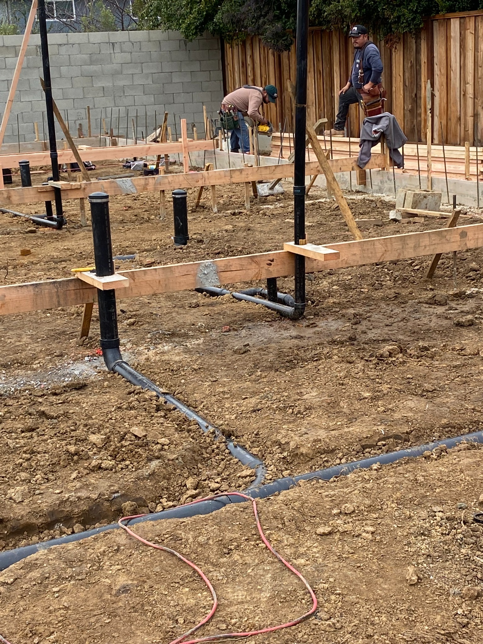 Construction site with exposed soil, underground pipework, timber forms and foundation reinforcement.