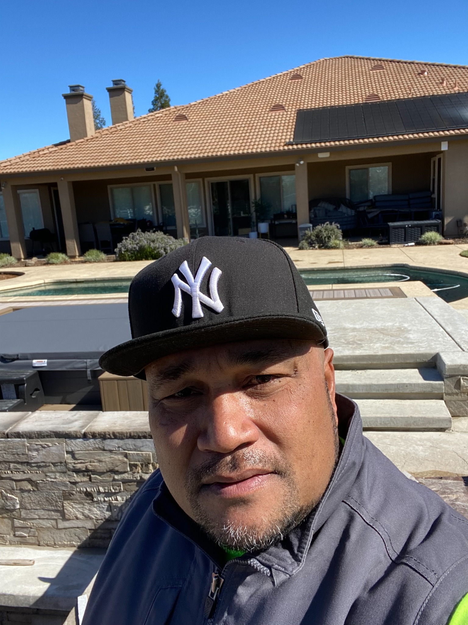 The owner of TMJ Builders Inc wearing a black cap, with a patio and pool behind him.