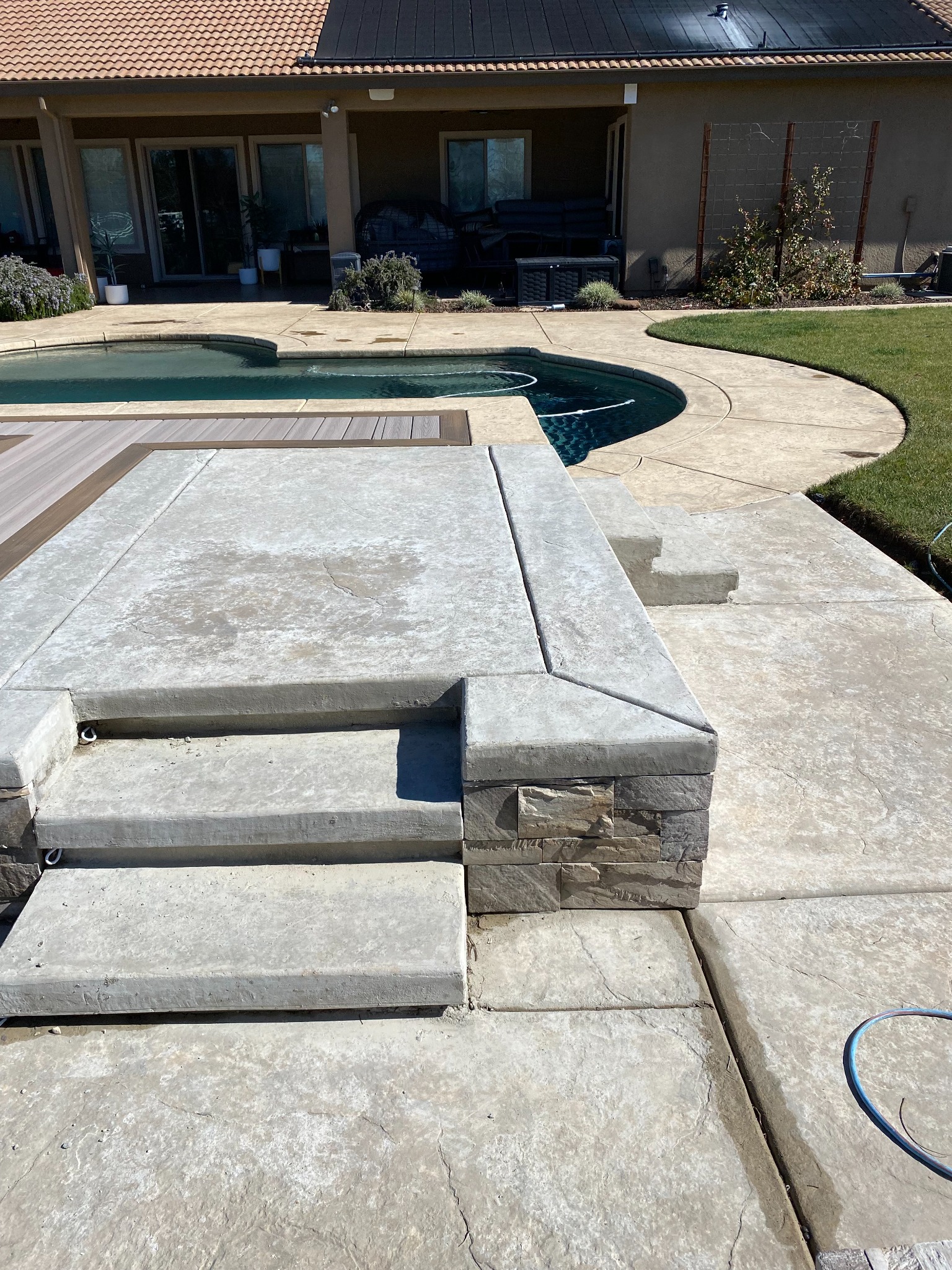 Concrete patio steps beside a stone-faced wall, swimming pool and decking.
